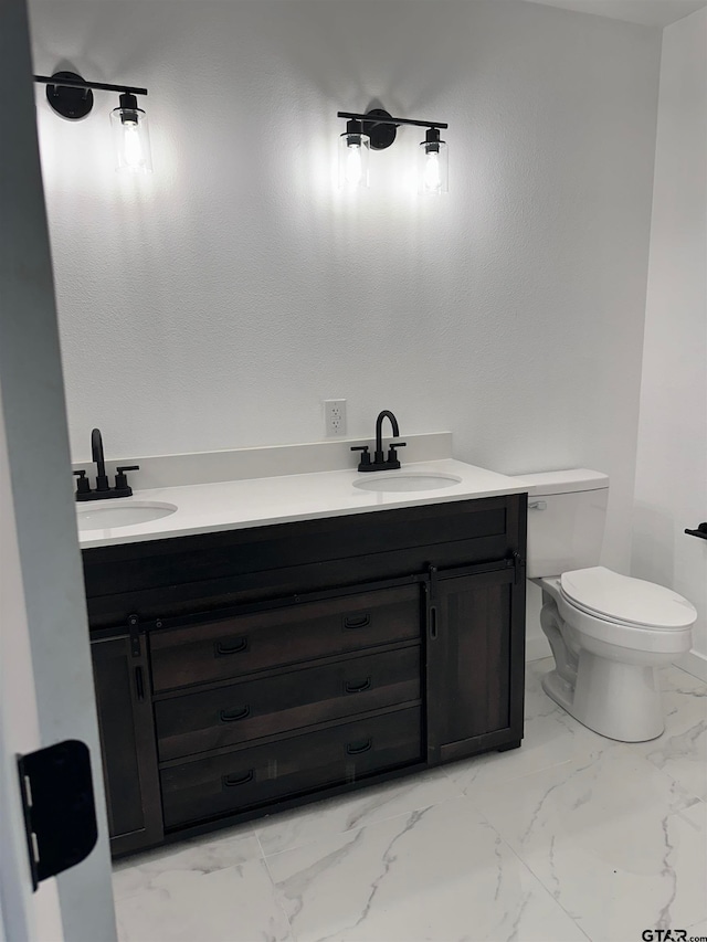 full bathroom with marble finish floor, double vanity, a sink, and toilet