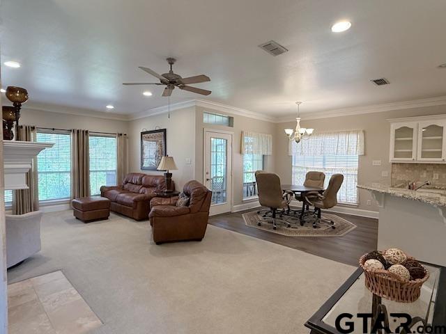 living room featuring carpet, ceiling fan with notable chandelier, a wealth of natural light, and ornamental molding