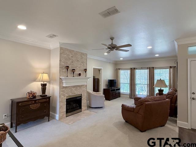 living room with a tile fireplace, ceiling fan, carpet floors, and ornamental molding