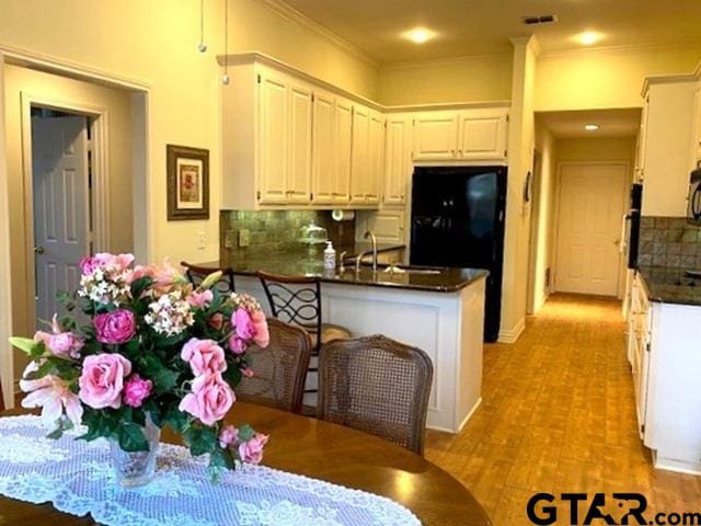 kitchen featuring tasteful backsplash, dark countertops, light wood-style flooring, ornamental molding, and a peninsula