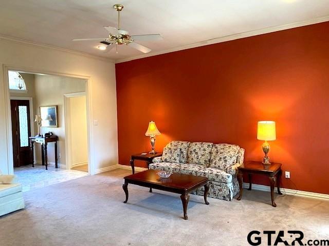 living room with a ceiling fan, baseboards, ornamental molding, and carpet flooring