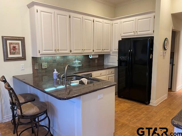 kitchen featuring white cabinets, a sink, a peninsula, and black fridge