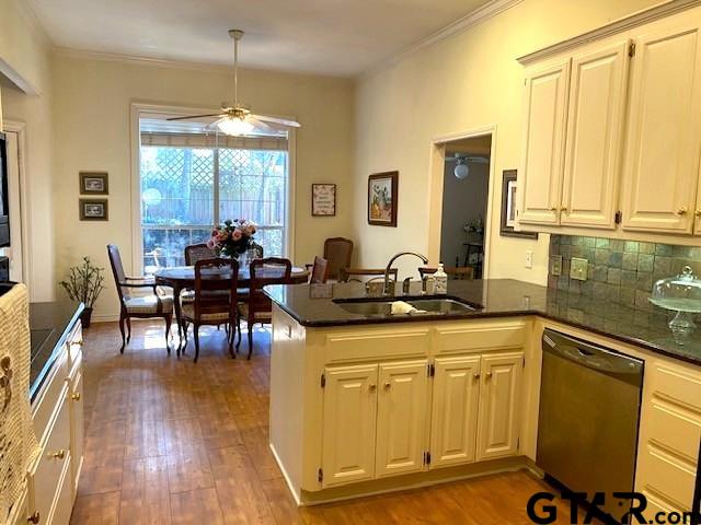 kitchen with wood finished floors, a peninsula, stainless steel dishwasher, and a sink