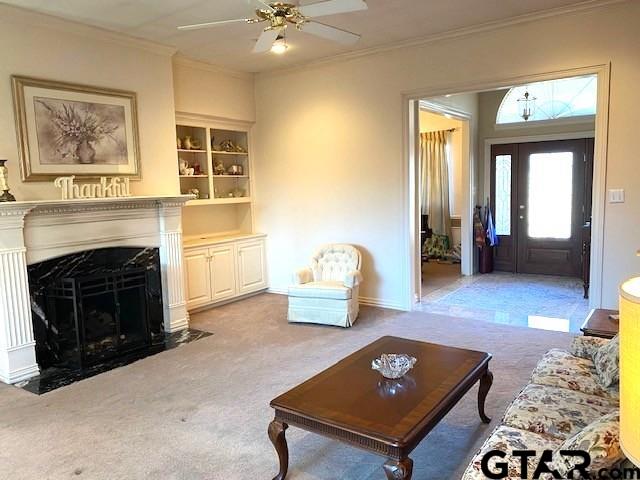 carpeted living room featuring a high end fireplace, crown molding, and ceiling fan