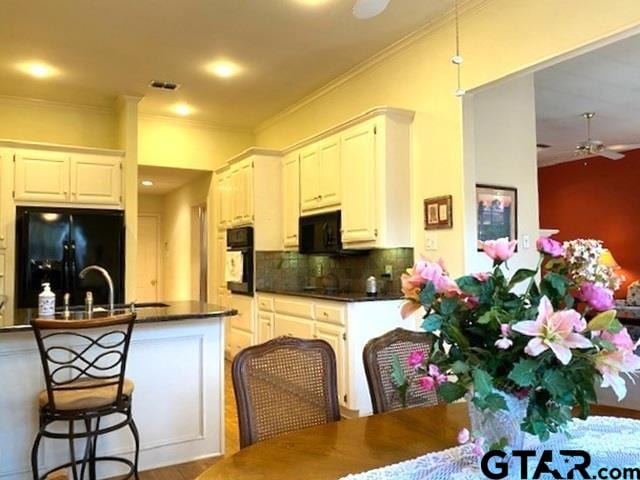 kitchen with decorative backsplash, dark countertops, crown molding, black appliances, and a sink