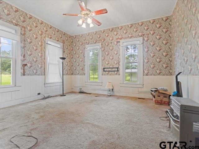 unfurnished room with crown molding, wainscoting, ceiling fan, wallpapered walls, and carpet flooring