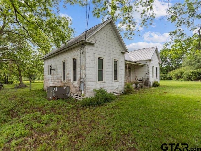view of property exterior with a lawn, cooling unit, and metal roof