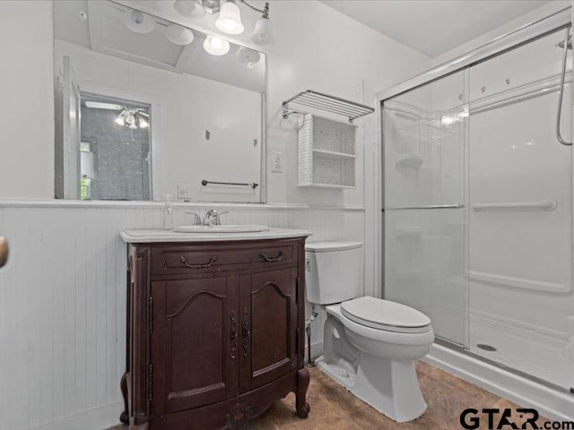 bathroom with toilet, a shower stall, and a wainscoted wall