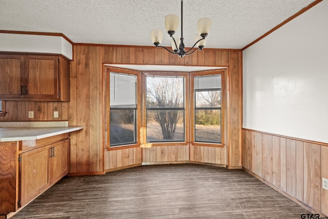 unfurnished dining area with wood walls, a textured ceiling, ornamental molding, dark hardwood / wood-style flooring, and a notable chandelier