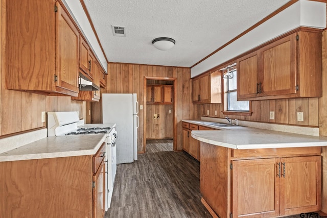 kitchen featuring wooden walls, dark hardwood / wood-style flooring, ornamental molding, white appliances, and a textured ceiling