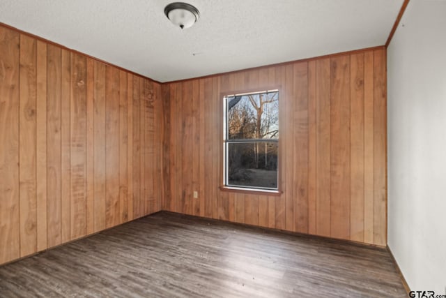 empty room featuring a textured ceiling, dark hardwood / wood-style flooring, and wood walls