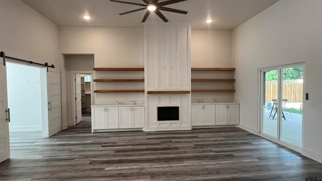 unfurnished living room with a high ceiling, dark wood-type flooring, a barn door, and ceiling fan