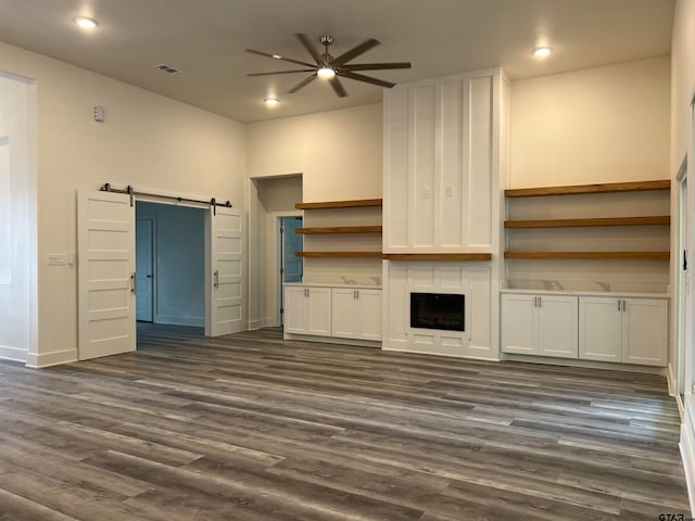 unfurnished living room with dark wood-type flooring, a barn door, and ceiling fan