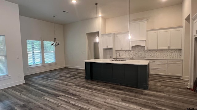 kitchen with a center island with sink, white cabinetry, backsplash, sink, and dark wood-type flooring