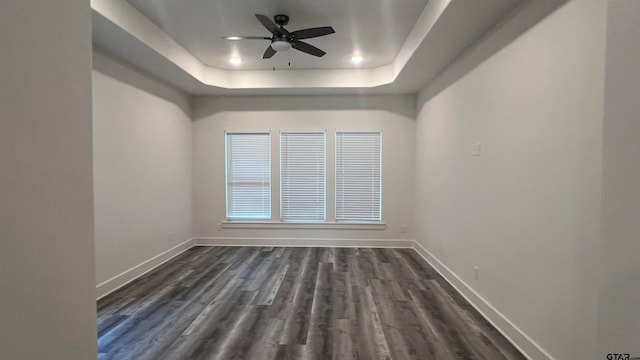 unfurnished room featuring dark wood-type flooring, a tray ceiling, and ceiling fan