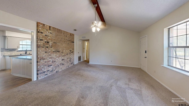 unfurnished living room with a healthy amount of sunlight, light carpet, and lofted ceiling with beams