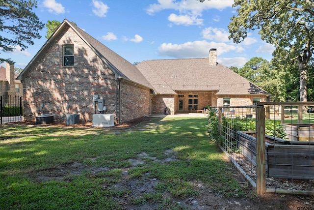 rear view of property with central AC unit, fence, a yard, a chimney, and brick siding