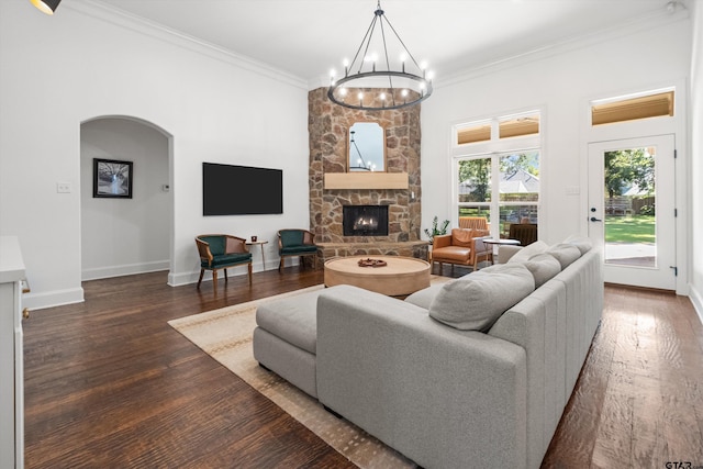 living room featuring dark wood-style floors, a stone fireplace, crown molding, and an inviting chandelier