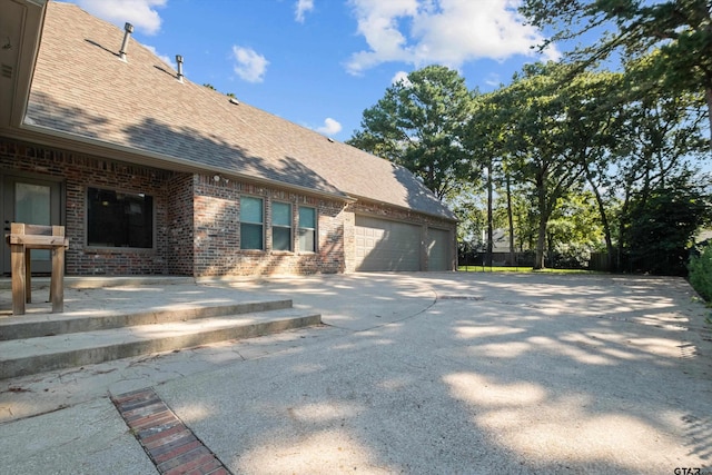 view of home's exterior with concrete driveway, an attached garage, brick siding, and a shingled roof