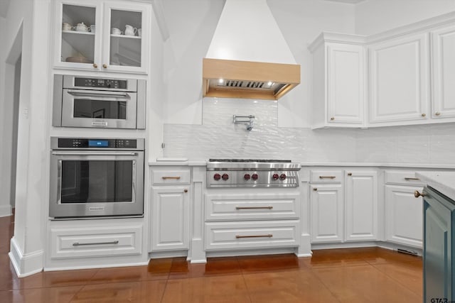 kitchen featuring stainless steel gas cooktop, dark tile patterned flooring, light countertops, custom range hood, and white cabinetry