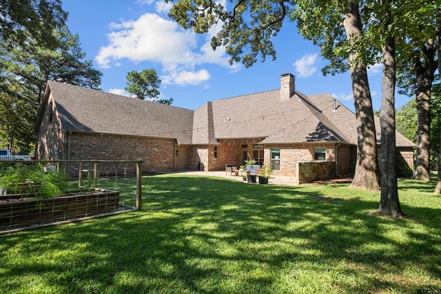 rear view of house featuring roof with shingles, a vegetable garden, brick siding, a patio area, and a lawn