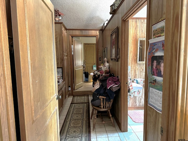 hallway with ornamental molding, a textured ceiling, wood walls, and light tile patterned floors