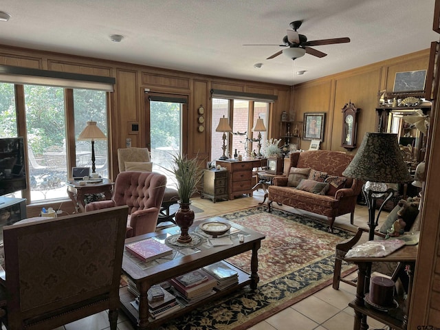 tiled living room featuring wood walls, ceiling fan, a textured ceiling, and a healthy amount of sunlight