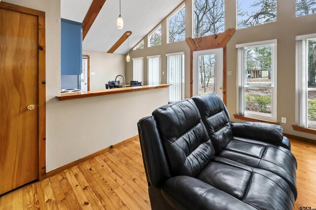 living room with beamed ceiling, light hardwood / wood-style floors, sink, and high vaulted ceiling