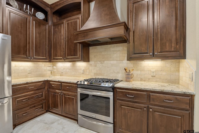 kitchen featuring dark brown cabinetry, backsplash, appliances with stainless steel finishes, light stone countertops, and custom exhaust hood