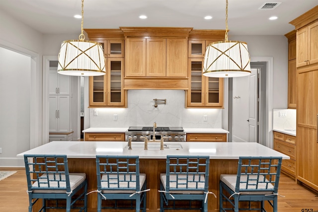 8810 Wilder Trl, Tyler, TX 75703 - kitchen with light wood-type flooring, light countertops, recessed lighting, glass insert cabinets, and a kitchen island with sink