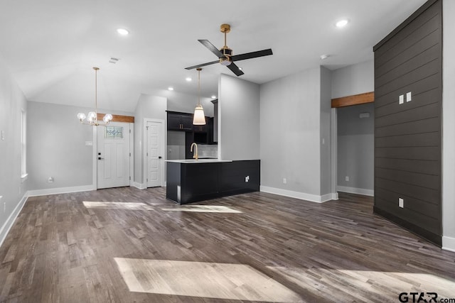 unfurnished living room featuring ceiling fan with notable chandelier, dark hardwood / wood-style flooring, sink, and vaulted ceiling