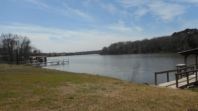 dock area featuring a forest view, a water view, and a lawn