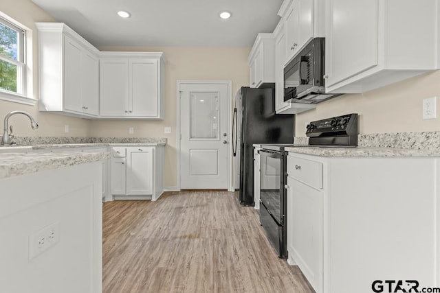 kitchen featuring black appliances, white cabinetry, light stone counters, and light hardwood / wood-style floors