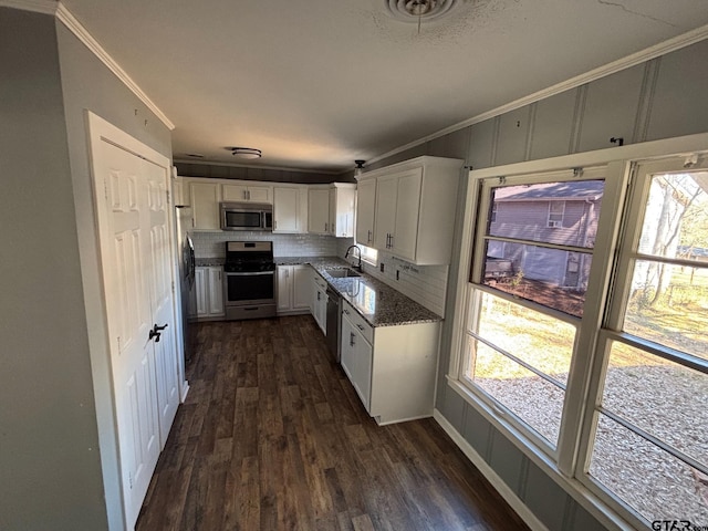 kitchen with stainless steel appliances, dark wood-type flooring, ornamental molding, white cabinetry, and a sink