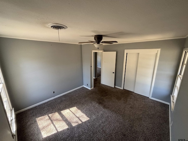 unfurnished bedroom with visible vents, dark carpet, ornamental molding, a textured ceiling, and baseboards