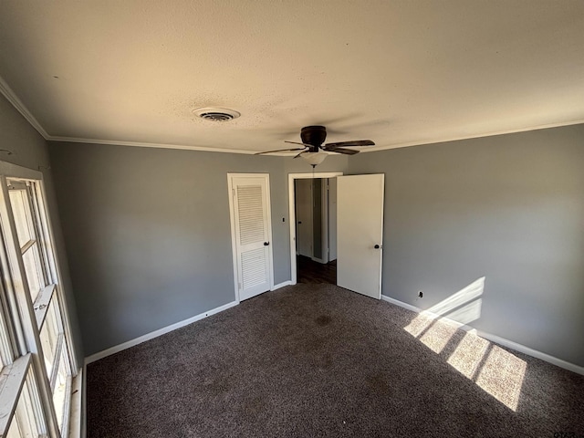 spare room with crown molding, dark colored carpet, visible vents, a textured ceiling, and baseboards