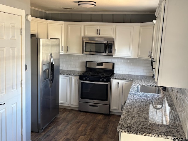 kitchen with appliances with stainless steel finishes, dark wood finished floors, dark stone countertops, and ornamental molding