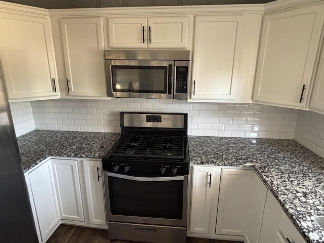 kitchen featuring dark stone counters, stainless steel appliances, white cabinets, and decorative backsplash