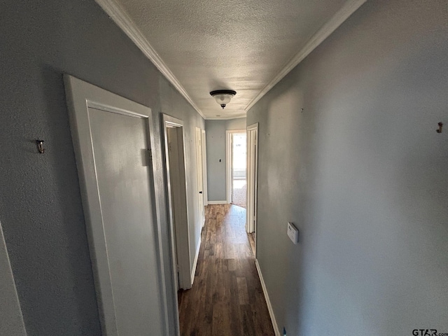 hall featuring a textured ceiling, baseboards, dark wood-style floors, and crown molding