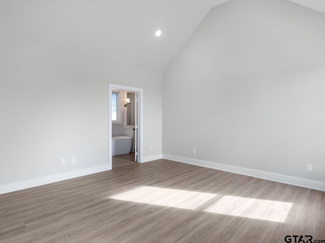 unfurnished bedroom featuring ensuite bathroom, light hardwood / wood-style floors, and high vaulted ceiling