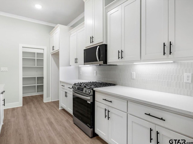 kitchen featuring white cabinetry, stainless steel gas stove, light wood-type flooring, decorative backsplash, and ornamental molding