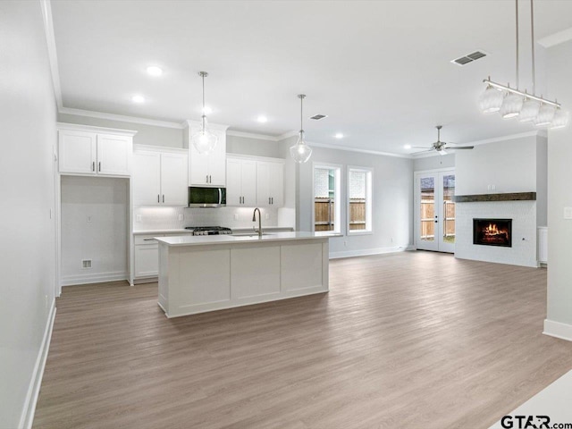 kitchen with white cabinetry, ceiling fan, light hardwood / wood-style floors, decorative light fixtures, and a center island with sink