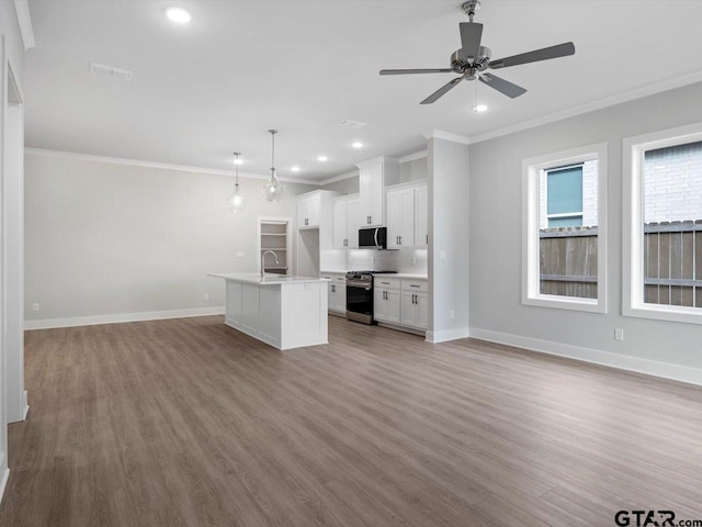 kitchen with hanging light fixtures, stainless steel gas range oven, a center island with sink, white cabinets, and ornamental molding