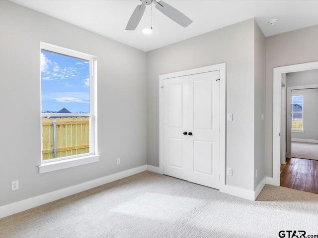 unfurnished bedroom with multiple windows, a closet, light colored carpet, and ceiling fan