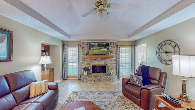 living room featuring baseboards, a ceiling fan, a raised ceiling, and a brick fireplace