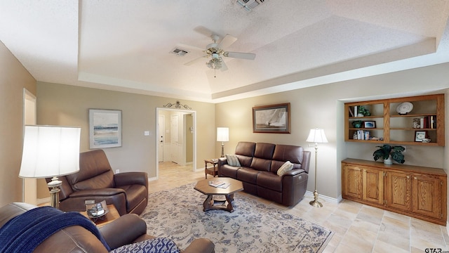 living room with ceiling fan, visible vents, baseboards, and a raised ceiling