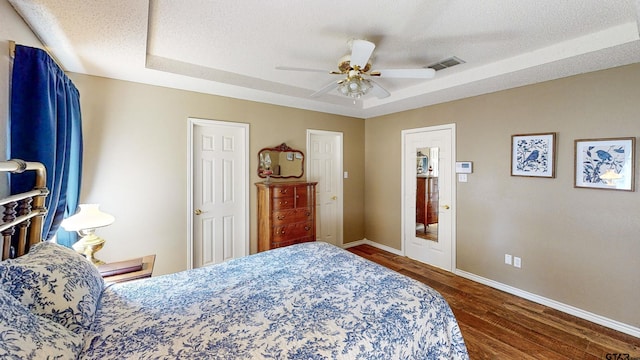 bedroom with baseboards, visible vents, wood finished floors, and a raised ceiling
