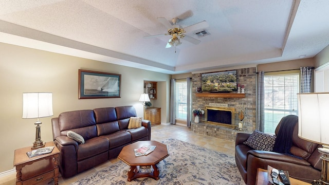 living area with visible vents, a fireplace, baseboards, a tray ceiling, and a ceiling fan