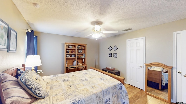 bedroom featuring light wood-type flooring, a ceiling fan, a textured ceiling, and visible vents