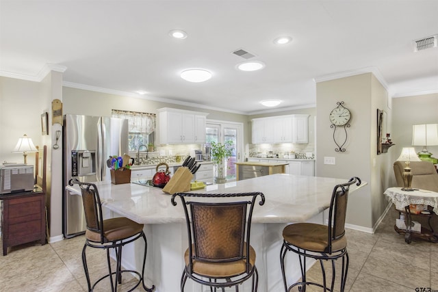 18058 Whispering Pines Rd, Flint, TX 75762 - kitchen featuring stainless steel refrigerator with ice dispenser, a center island, backsplash, a breakfast bar area, and white cabinetry